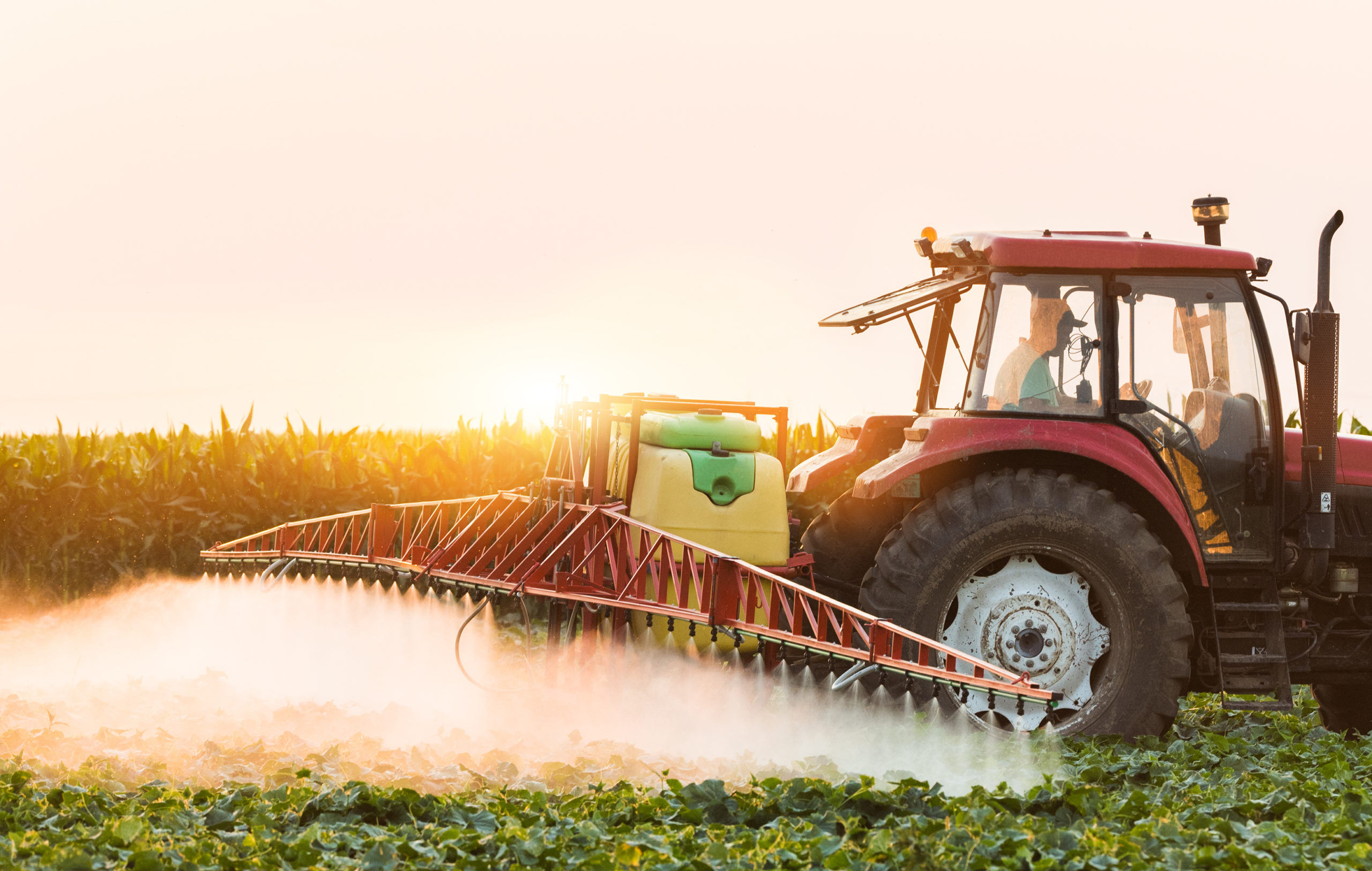 Tractor spraying pesticides on field with sprayer