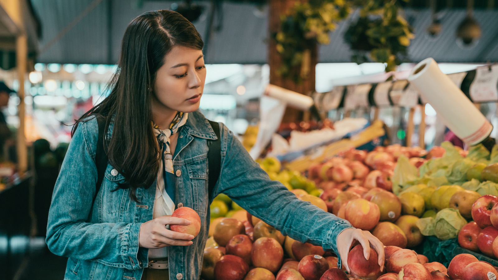 Asian woman wearing a denim jacket picking peaches in supermarket