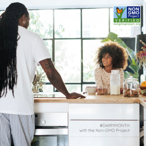 African American man with dreadlocks standing facing his back in a kitchen with his young daughter sitting at the kitchen counter and there's a milk carfe on the table