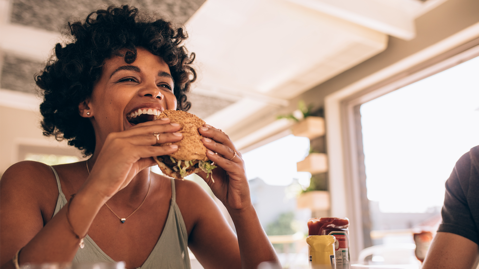 African woman eating stack burger at restaurant with friends.